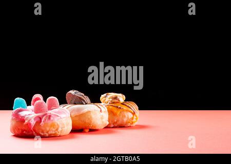 Fotografia di tre ciambelle decorate con biscotti al cioccolato e fagioli di gelatina su una scheda rossa e uno sfondo nero.la fotografia ha spazio di copia ed è Foto Stock