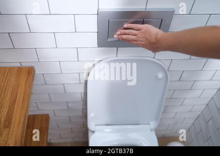 La mano femmina preme il pulsante di scarico nel primo piano della toilette Foto Stock