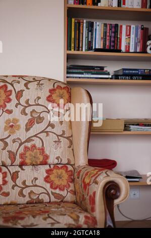 POZNAN, POLONIA - Nov 29, 2015: Una poltrona con motivi floreali accanto a ripiani in legno con libri Foto Stock