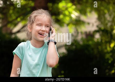 Bambino giovane età della scuola che parla sul suo cellulare, bambina che parla, tenendo uno smartphone accanto all'orecchio, smart band a mano ritratto primo piano, copia Foto Stock