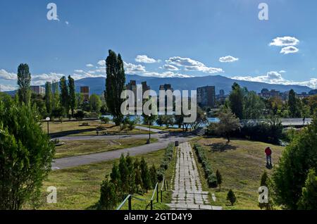 Panorama autunnale di parte del quartiere vicino al lago con alberi verdi, arbusti e erba solare, Drujba, Sofia, Bulgaria Foto Stock