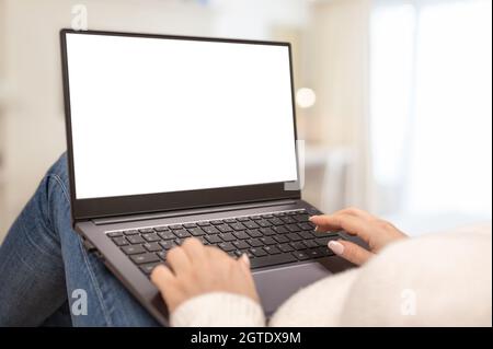 immagine mockup schermo computer portatile vuoto con sfondo bianco vuoto per la pubblicità di testo. Donna che guarda il mock up bianco schermo sdraiato sul divano Foto Stock