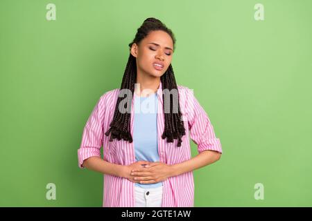 Foto di malsano pelle scura signora indossare camicia rosa braccia stomaco avere dolore isolato sfondo verde colore Foto Stock