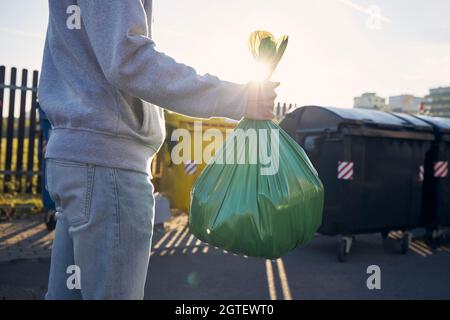 Uomo che cammina con rifiuti. Portare a mano il sacchetto di plastica contro i bidoni della spazzatura sulla strada. Foto Stock