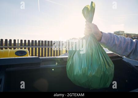 Uomo che cammina con rifiuti. Portare a mano il sacchetto di plastica contro i bidoni della spazzatura sulla strada. Foto Stock