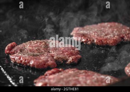 Processo di cottura degli cheeseburgers sul grill. Primo piano hamburger di carne di manzo per hamburger Foto Stock