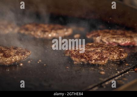 Processo di cottura degli cheeseburgers sul grill. Primo piano hamburger di carne di manzo per hamburger Foto Stock