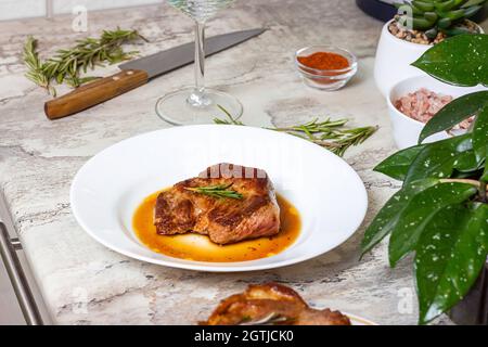 Bistecca di manzo arrosto preparata con spezie e rosmarino su piatto rotondo bianco sullo sfondo del tavolo da cucina. Foto Stock