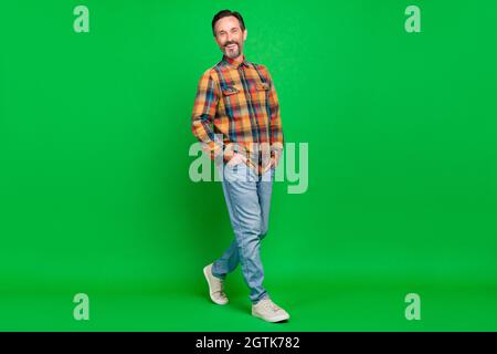 Vista a tutta lunghezza del corpo dell'attraente uomo allegro che passeggava isolato su sfondo di colore verde chiaro Foto Stock