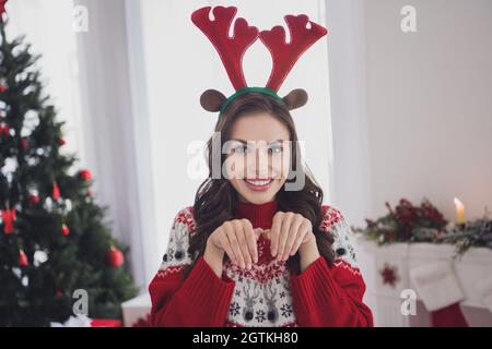 Foto di funky allegra ragazza allegra pretendere renna indossare corna fasciatesta maglione in casa decorata interni Foto Stock