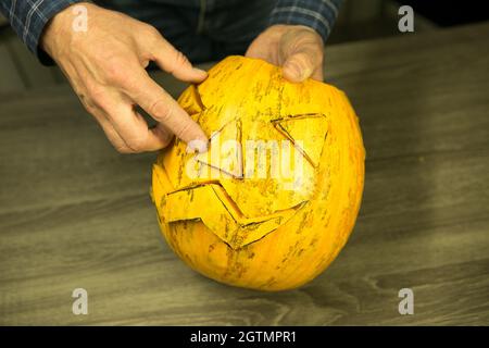 Come fare a casa Jack o'Lantern? Mani maschili con coltello, avanzi di zucca sul tavolo da cucina. Messa a fuoco selettiva e bokeh. Foto Stock