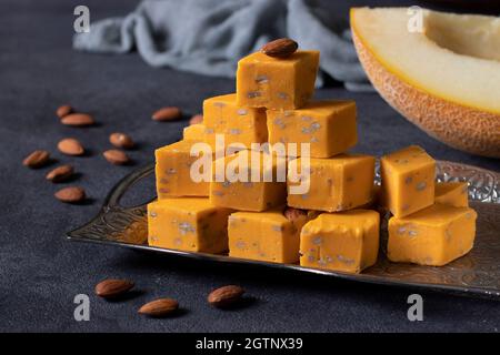 Deliziose fette di halva di latte orientale con aroma di melone, semi di girasole e mandorle su sfondo scuro. I dolci tradizionali artigianali uzbeki. Foto Stock