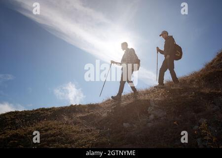 Due silhouette uomo che camminano lungo la cima della montagna con zaini da trekking si incontrano i raggi del sole e il cielo blu sfondo Foto Stock