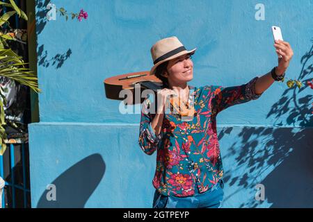 Donna musicista con una chitarra che fa una foto con il suo telefono cellulare su una strada Foto Stock