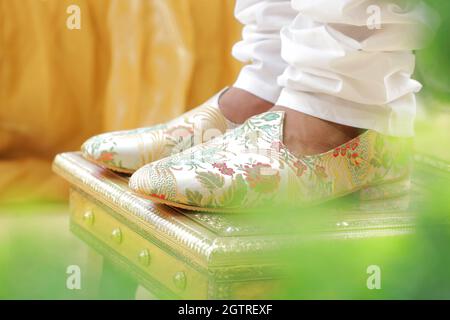 Immagina una scena vivace sotto un mandap splendidamente decorato, dove la coppia felice si siede fianco a fianco, irradiando gioia. La sposa, riccamente adornata Foto Stock