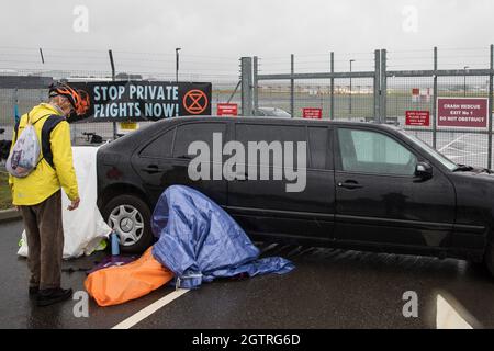 Farnborough, Regno Unito. 2 ottobre 2021. Un attivista climatico della Rebellion d'estinzione siede bloccato su una limousine stretch che blocca un ingresso all'Aeroporto di Farnborough. Gli attivisti hanno bloccato tre ingressi all'aeroporto privato per evidenziare livelli elevati di anidride carbonica prodotti dai passeggeri super ricchi che utilizzano jet privati e il lavaggio del verde da parte dell'aeroporto, annunciando il passaggio al carburante per aviazione sostenibile (SAF). Credit: Mark Kerrison/Alamy Live News Foto Stock