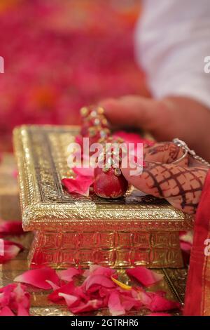 Immagina una scena vivace sotto un mandap splendidamente decorato, dove la coppia felice si siede fianco a fianco, irradiando gioia. La sposa, riccamente adornata Foto Stock