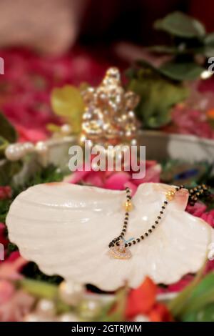 Immagina una scena vivace sotto un mandap splendidamente decorato, dove la coppia felice si siede fianco a fianco, irradiando gioia. La sposa, riccamente adornata Foto Stock