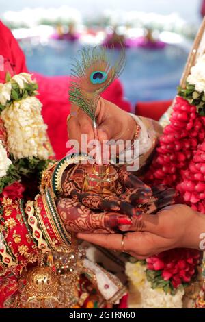 Immagina una scena vivace sotto un mandap splendidamente decorato, dove la coppia felice si siede fianco a fianco, irradiando gioia. La sposa, riccamente adornata Foto Stock