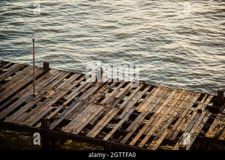 Vecchio e abbandonato molo di legno con il sole del pomeriggio che splende su di esso. Foto Stock