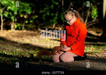 Una ragazza con la sindrome di Down nutre una noce scoiattolo nella foresta al tramonto Foto Stock