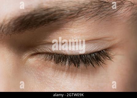 Primo piano di un occhio umano chiuso, sopracciglia spessa maschile e ciglia lunghe Foto Stock