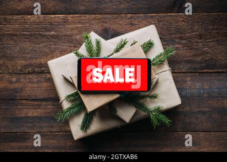 Vendita di Natale, shopping online di Natale, vendita vacanze invernali, Black Friday. Telefono delle cellule con il testo di vendita dello schermo rosso sulla pila delle scatole del regalo di natale con Foto Stock