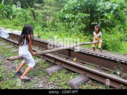 Due giovani ragazze che giocano su vecchi binari del treno usando un vecchio palo di legno come una sega a vista improvvisata a Lembah Anai, Sumatra Occidentale, Indonesia. Foto Stock