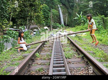 Due giovani ragazze che giocano su vecchi binari del treno usando un vecchio palo di legno come una sega a vista improvvisata a Lembah Anai, Sumatra Occidentale, Indonesia. Foto Stock