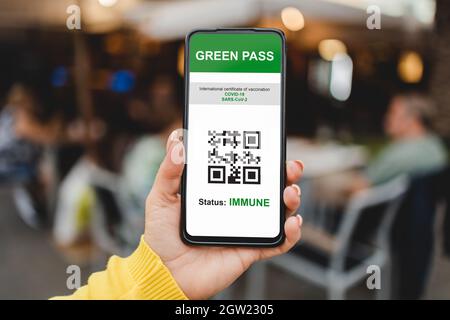 Certificato di Green pass digitale immunitario per il vaccino contro il coronavirus con bar ristorante sullo sfondo - Focus su donna mano che tiene il telefono cellulare Foto Stock