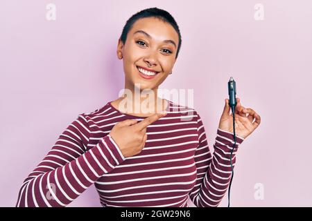 Bella ispanica donna con capelli corti tenendo usb adattatore caricabatterie per l'auto sorridente felice di puntare con mano e dito Foto Stock