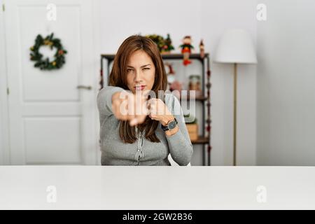 Giovane donna latina seduta sul tavolo da natale decoro punzonando pugno a combattere, attacco aggressivo e arrabbiato, minaccia e violenza Foto Stock