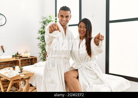 Giovane coppia latina che indossa un asciugamano in piedi al centro di bellezza puntando a te e la macchina fotografica con le dita, sorridendo positivo e allegro Foto Stock