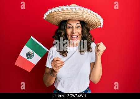 Donna ispanica in Medio Evo che indossa cappello messicano che regge bandiera del messico urlando orgoglioso, celebrando la vittoria e il successo molto eccitato con braccio sollevato Foto Stock