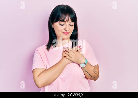 Giovane donna ispanica che indossa abiti casual sorridendo con le mani sul petto con gli occhi chiusi e gesto grato sul viso. Concetto di salute. Foto Stock