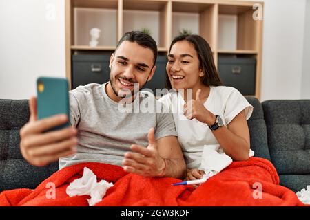 Giovane coppia malata latina che ha teleconsulto medico utilizzando smartphone a casa. Foto Stock