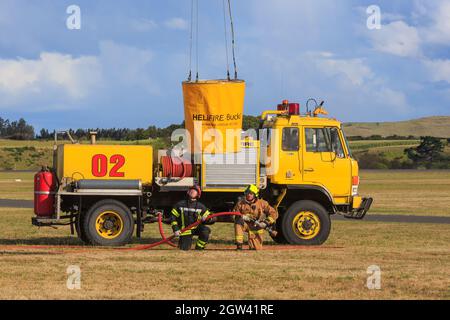 Un camion dei pompieri in un aeroporto. Un secchio di monsone viene abbassato da un elicottero per riempire i vigili del fuoco Foto Stock