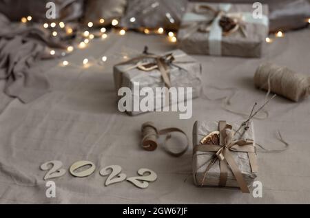 Sfondo di Natale con scatole regalo avvolto in carta artigianale e numeri di legno 2022 su sfondo sfocato con ghirlanda. Foto Stock
