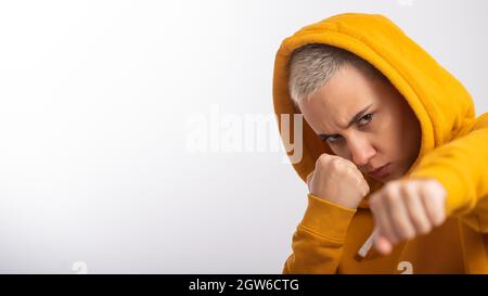 Giovane donna in cappa ocra che tiene i pugni vicino faccia su sfondo bianco. Boxer girl è pronta per una lotta. Foto Stock