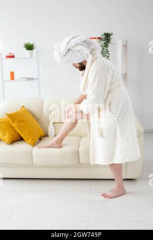 L'uomo bearded divertente sfrega la crema del corpo sulle sue gambe. Spa, cura del corpo e della pelle per l'uomo Foto Stock