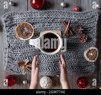 Composizione casalinga accogliente con una tazza di tè, le mani del bambino, elemento a maglia, dettagli decorativi di natale, posa piatta. Foto Stock