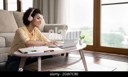 Sorridente giovane donna africana in cuffie che studia a casa. Foto Stock