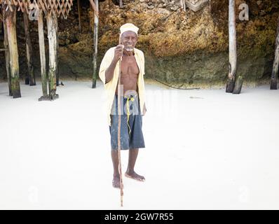 shepard africano invecchiato camminando sulla spiaggia tenendo bastone Foto Stock
