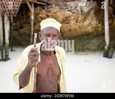 shepard africano invecchiato camminando sulla spiaggia tenendo bastone Foto Stock