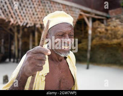 shepard africano invecchiato camminando sulla spiaggia tenendo bastone Foto Stock