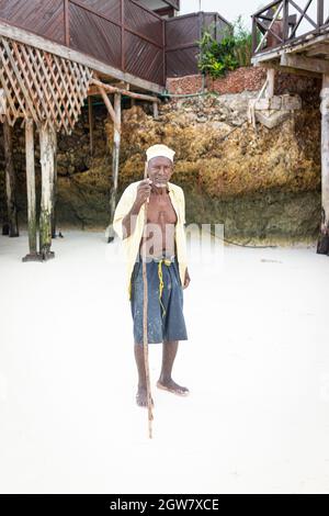 shepard africano invecchiato camminando sulla spiaggia tenendo bastone Foto Stock
