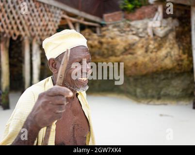 shepard africano invecchiato camminando sulla spiaggia tenendo bastone Foto Stock