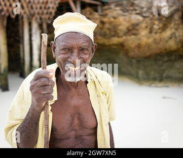 shepard africano invecchiato camminando sulla spiaggia tenendo bastone Foto Stock