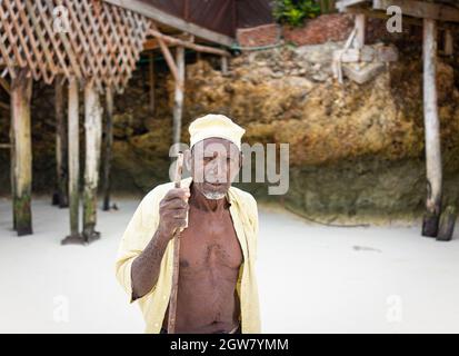 shepard africano invecchiato camminando sulla spiaggia tenendo bastone Foto Stock