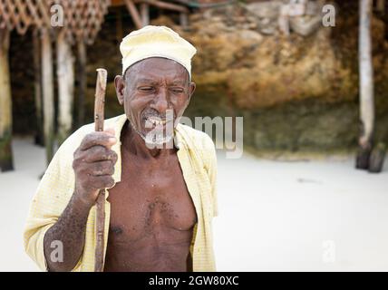 shepard africano invecchiato camminando sulla spiaggia tenendo bastone Foto Stock